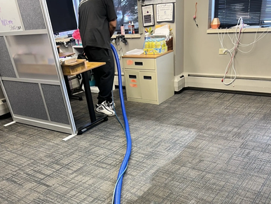 Person standing on a desk with a blue hose in an office setting.