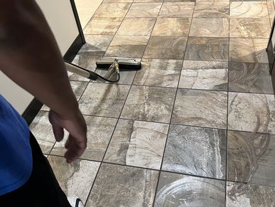 Person cleaning a tiled floor with a mop and cleaning solution.