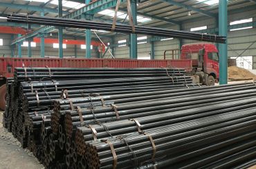 Stacks of black metal pipes inside an industrial warehouse.