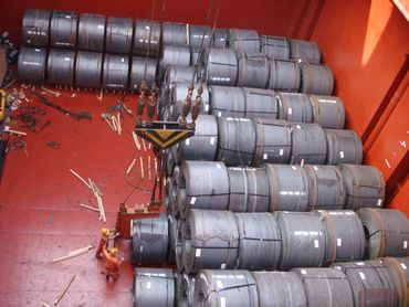 Steel coils stacked inside a cargo ship hold with workers nearby.