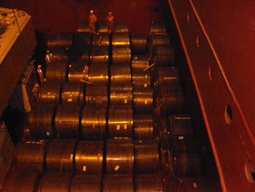 Workers inspecting large steel coils stacked in a warehouse or ship.