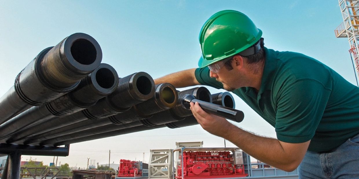 Worker inspecting threaded pipes with a flashlight at an industrial site.
