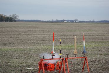 Model rockets launching from a field on a clear day.