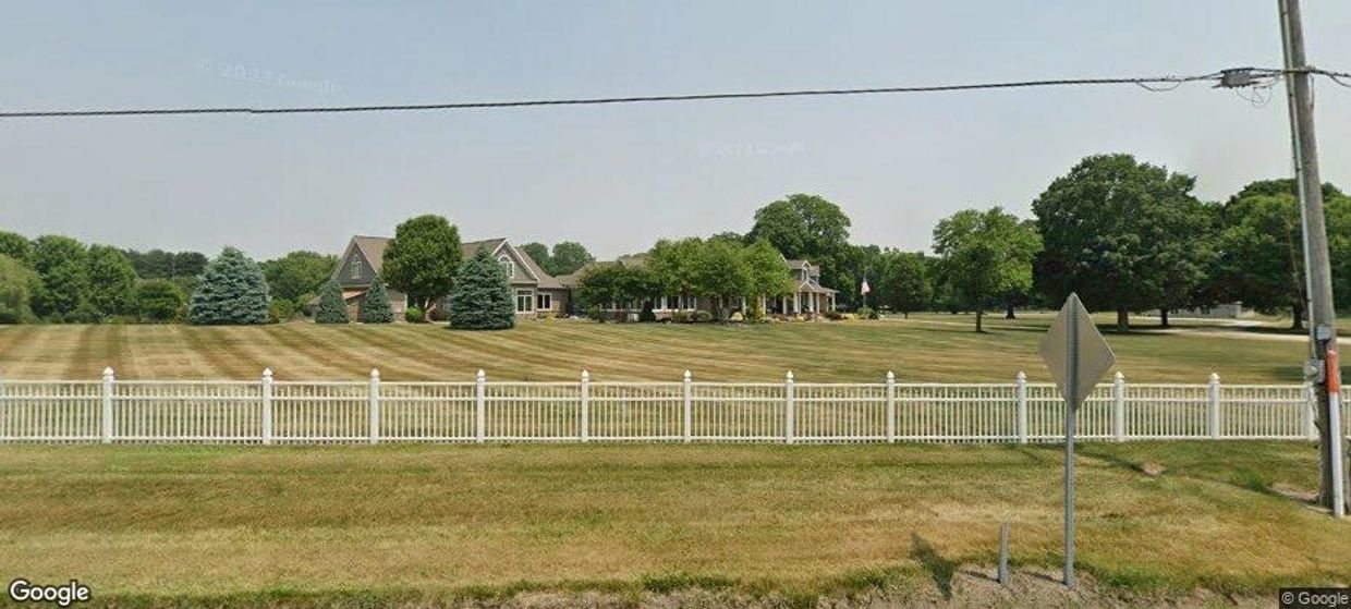 Large house with a big lawn and white fence.