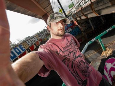 Young man taking a selfie under a graffiti-covered overpass.