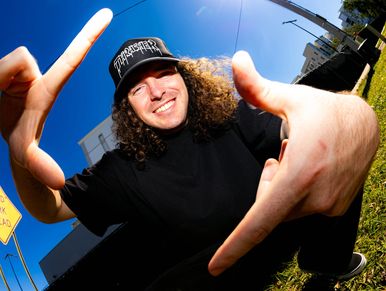 Man with curly hair framing his face with his hands, smiling outdoors.