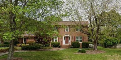 Two-story brick house surrounded by trees and greenery.