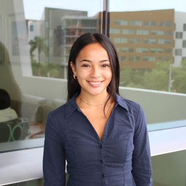 A smiling woman standing indoors near a window.