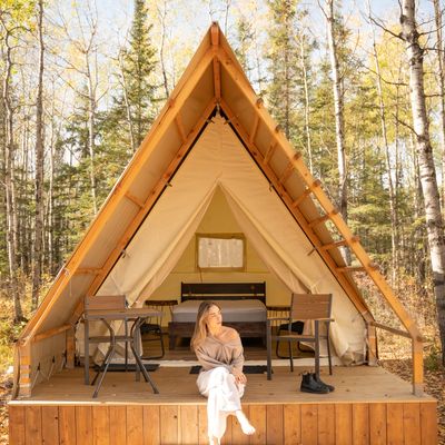 Woman sitting on porch of a cozy A-frame cabin in a forest.