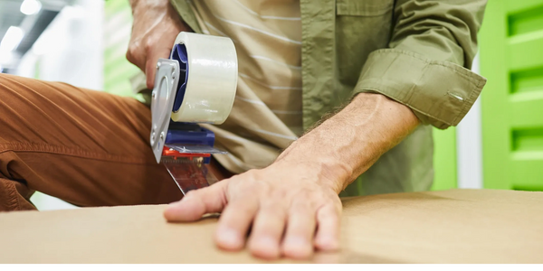 Photo of a mans hand sealing a cardboard box.
