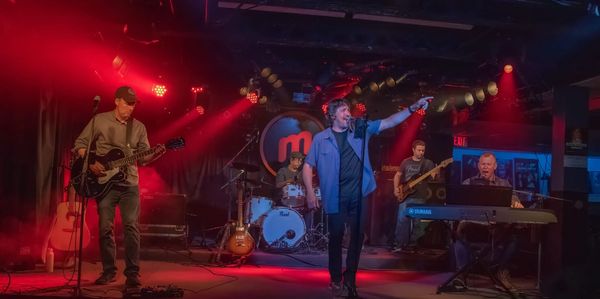 Band performing live on stage with vibrant red lighting.