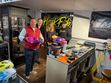Four people holding colorful remote control cars in a hobby workshop.
