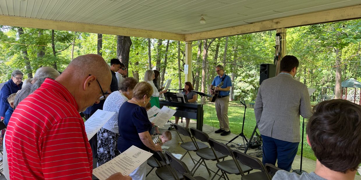 Group singing outdoors under a pavilion.