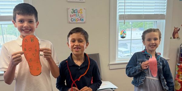 Three kids showing their crafts in a classroom.