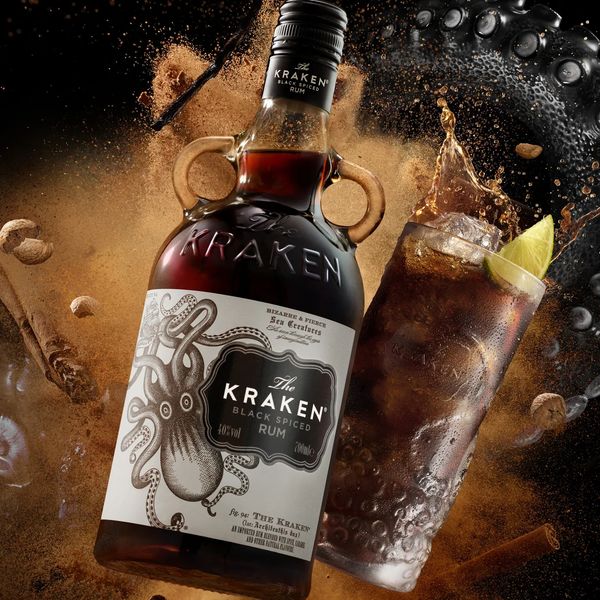 Bottle of The Kraken Black Spiced Rum with a mixed drink and lime wedge.