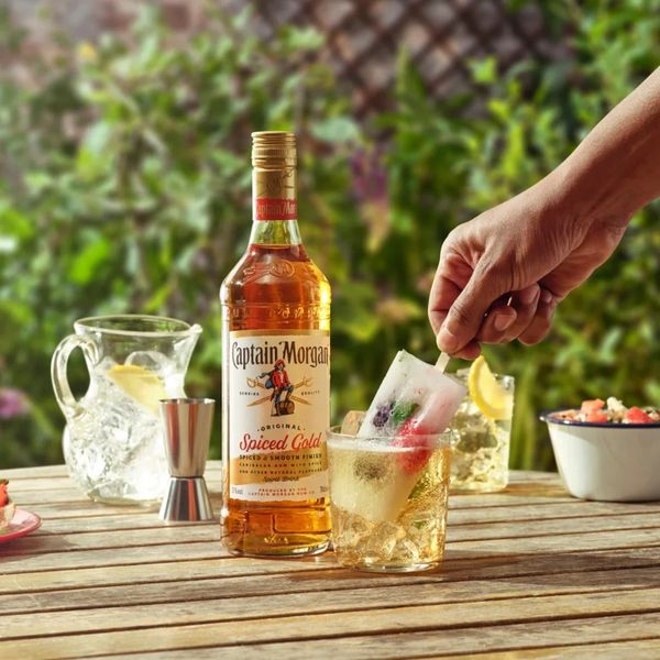 Bottle of Captain Morgan rum with a hand holding a popsicle in a glass with ice.