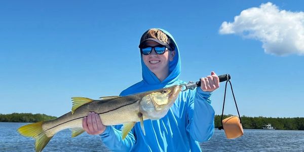 Person holding a large fish on a boat under clear blue sky.