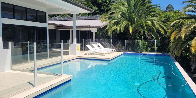Modern pool area with clear blue water and white loungers under palm trees.