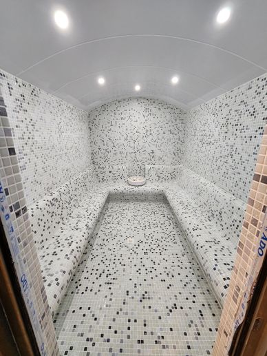 A spacious steam room with mosaic tile walls and ceiling lights.
