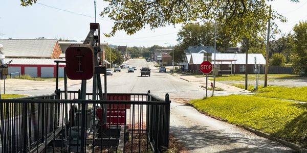 Small-town street with cars, a stop sign, and old machinery.