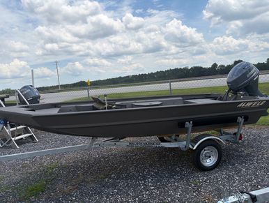 A small black fishing boat on a trailer under a cloudy sky.