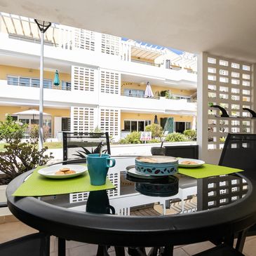 Outdoor patio table set with coffee and snacks in a sunny apartment complex.