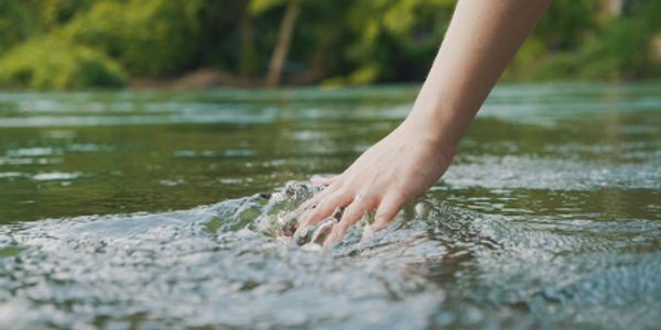 A hand gently touching the surface of a flowing river.