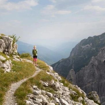 Person standing on mountain trail overlooking rocky cliffs.