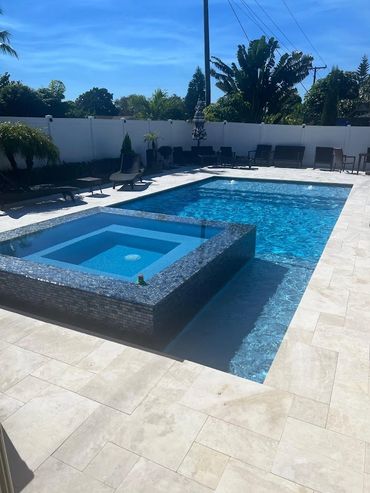 Modern backyard pool with an attached spa and lounge chairs under clear blue sky.