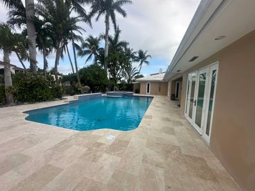 A modern backyard pool surrounded by palm trees and beige stone tiles.