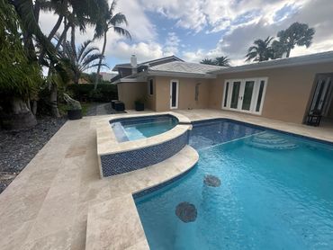 A modern backyard pool with a built-in hot tub and palm trees.