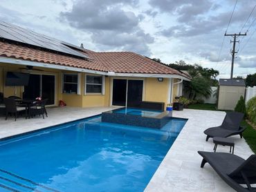 Modern backyard with a pool, spa, and lounge chairs under a cloudy sky.