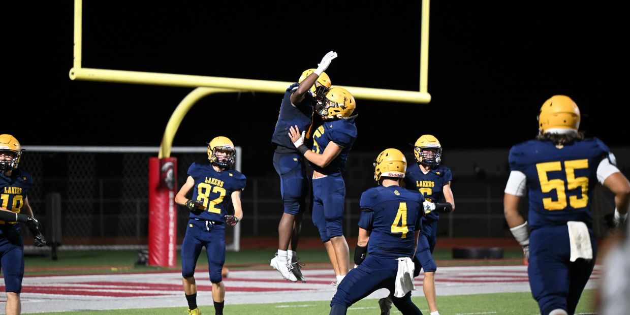 High school football players celebrating a touchdown under the goalpost at night.