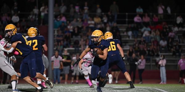 High school football player running with the ball during a night game.