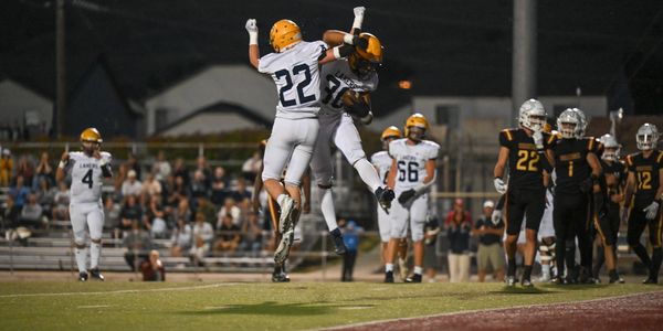Two football players in white celebrate with a mid-air chest bump during a night game.