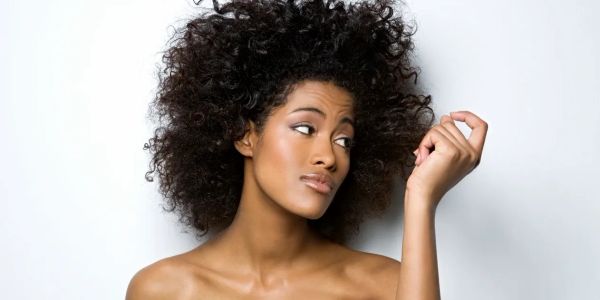 Woman with curly hair looking at her nails thoughtfully.