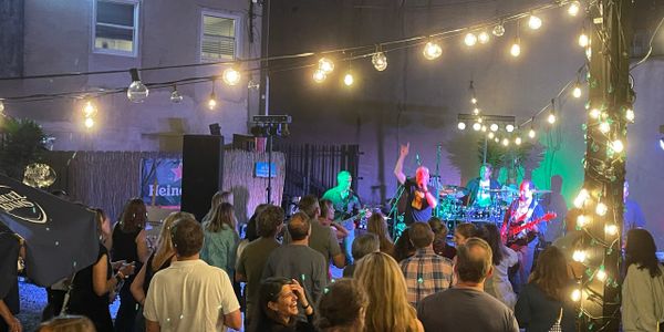 A lively outdoor concert with a band performing under string lights and an engaged crowd.