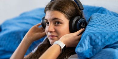 Young woman wearing headphones relaxing on a blue cushion.