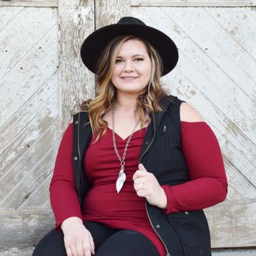Woman in a black hat and red top sitting against a rustic wooden door.