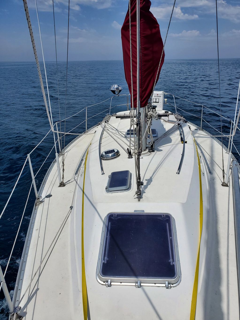 View from the deck of a sailboat on calm blue waters under a partly cloudy sky.