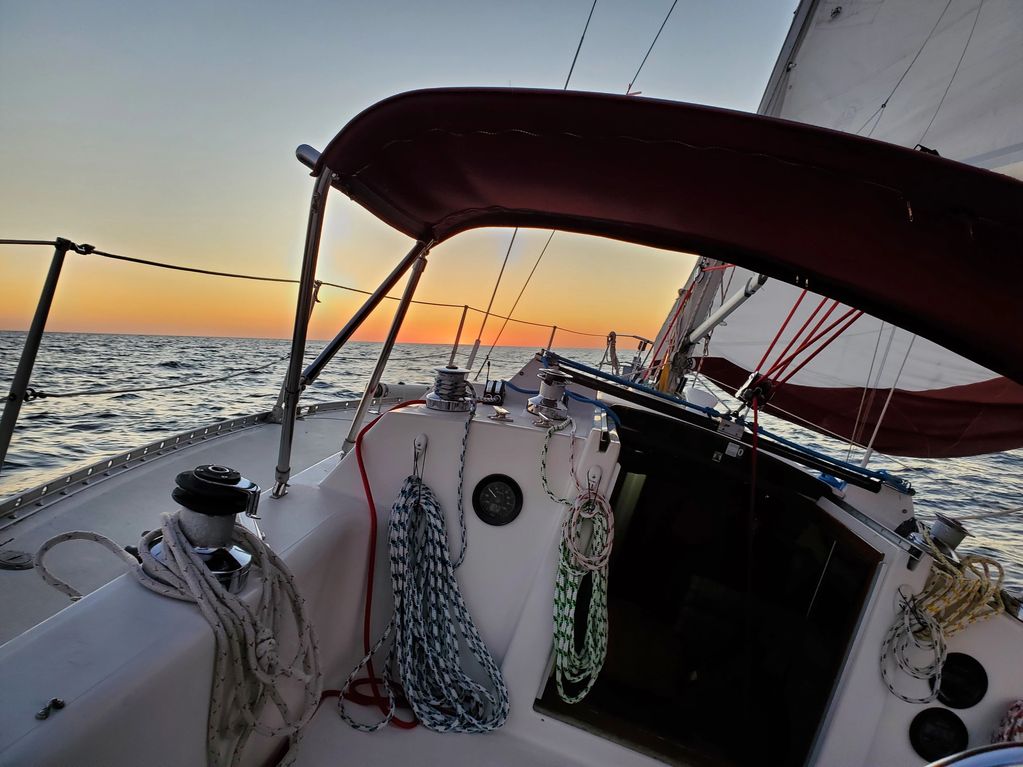 Sailing boat deck at sunset with coiled ropes and calm sea.