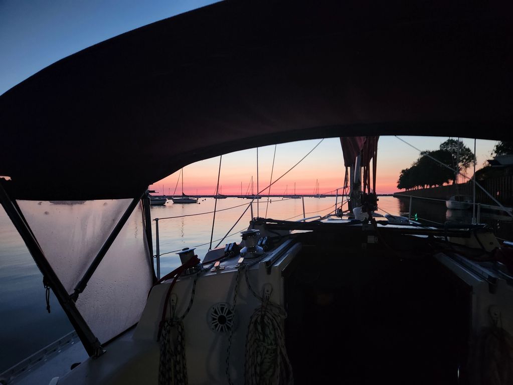 View from inside a boat at sunset over a calm harbor with anchored sailboats.