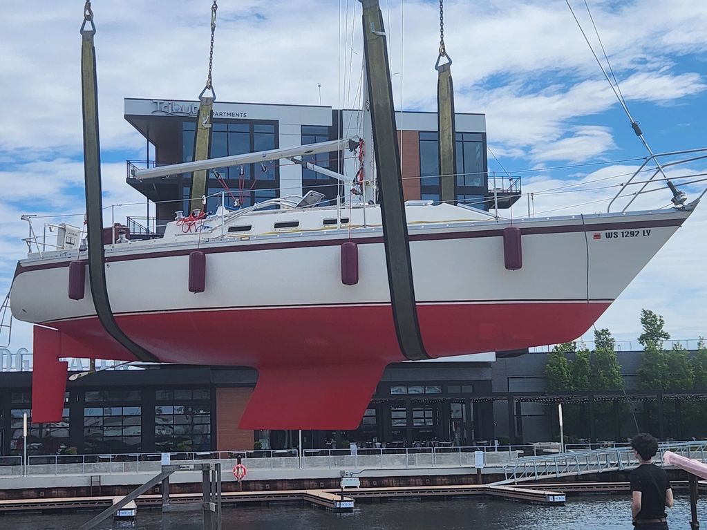 Sailboat with red bottom hull being lifted by crane at a marina.