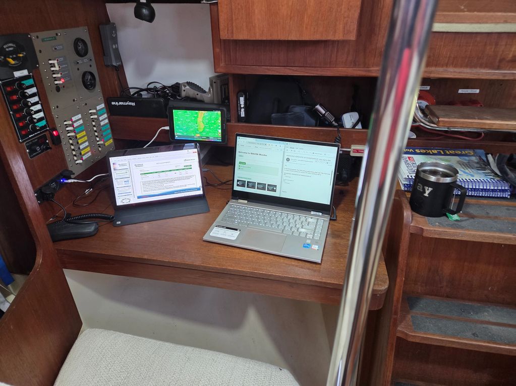 A workspace on a boat with two screens, navigation device, and coffee mug.