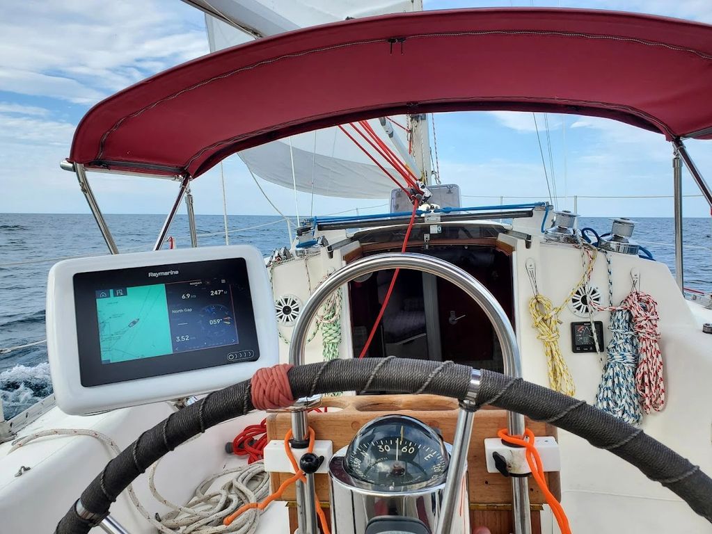 View from a sailboat's helm with navigation screen and ocean ahead.