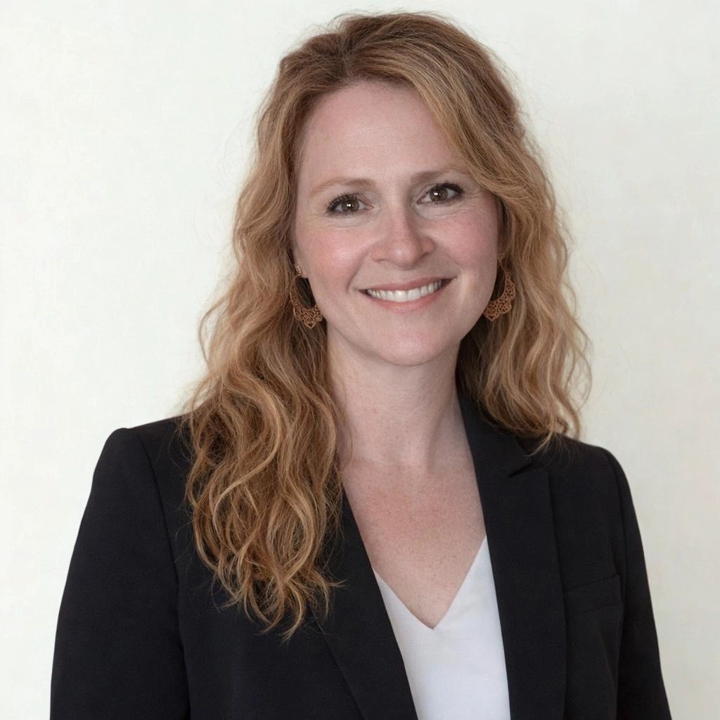 Smiling woman with wavy blonde hair in a black blazer and white top.