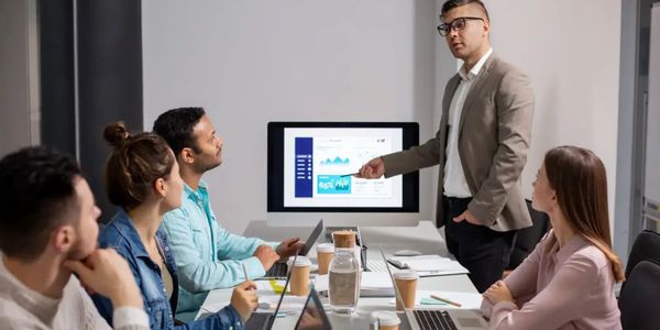 Man presenting data on screen to colleagues in a meeting room.