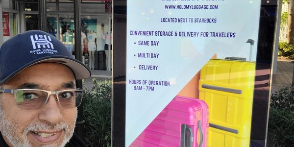Man posing next to a luggage storage service advertisement near Starbucks.