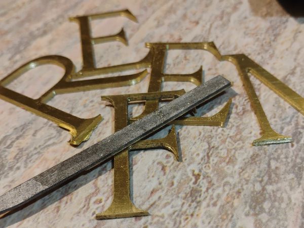 Metal letters and a file tool on a textured surface.