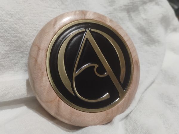 A round wooden plaque with a metallic symbol featuring a stylized letter A.